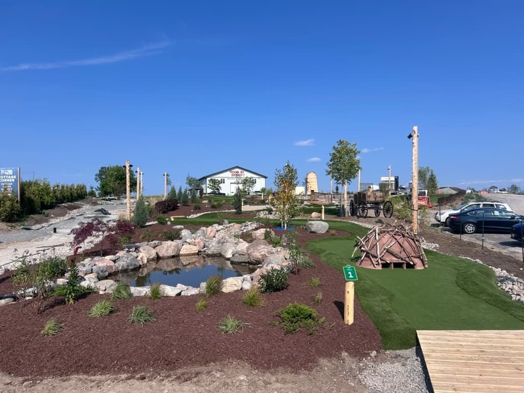 Hole 1 at The Little Mini Golf Co, with the pond, beaver lodge, and landscaped gardens